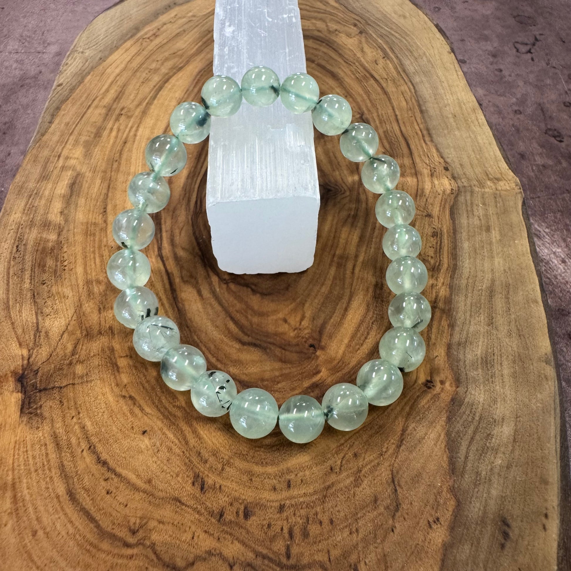 Green beaded bracelet on a wooden surface with a crystal in the background