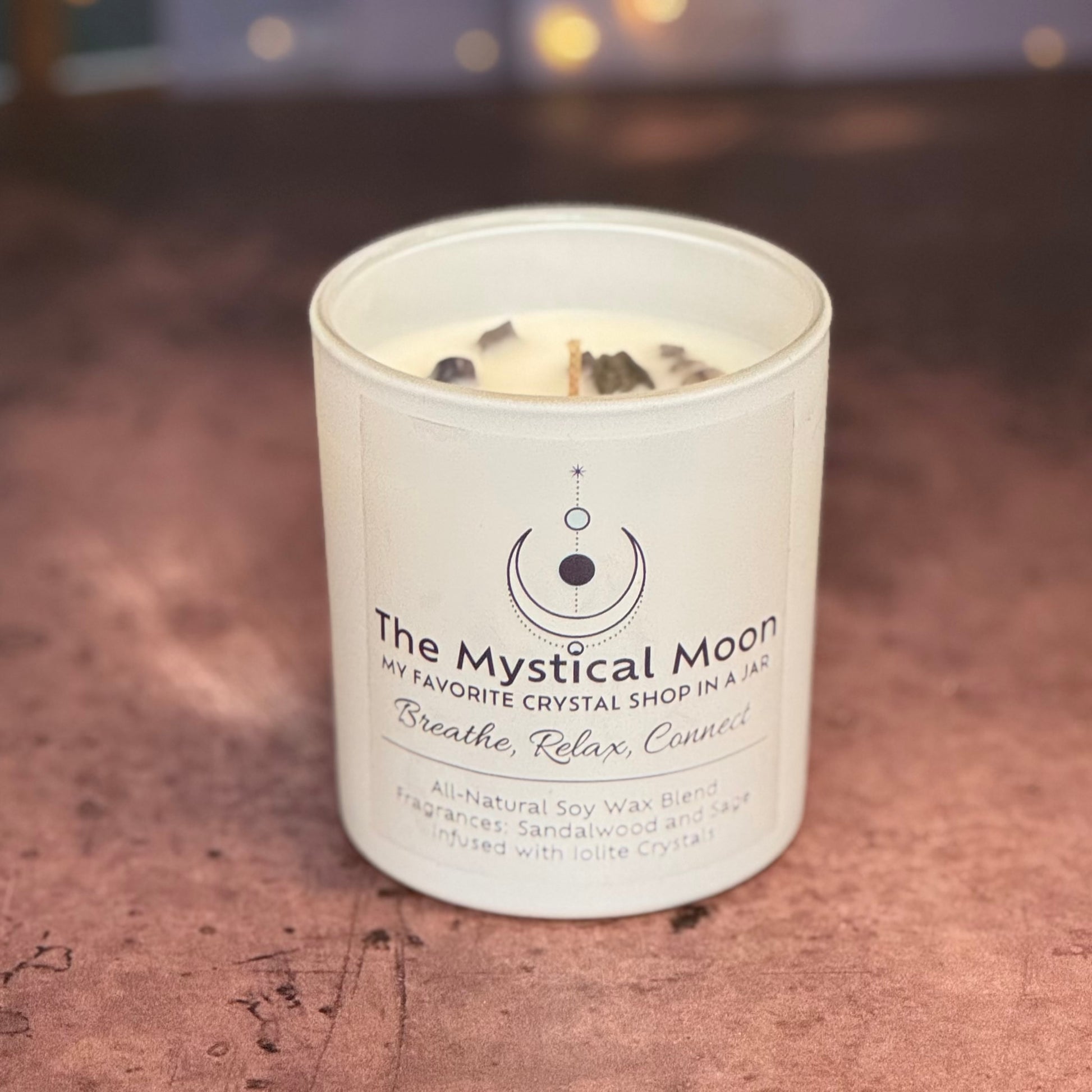 Candle in a jar labeled 'The Mystical Moon' on a wooden surface.