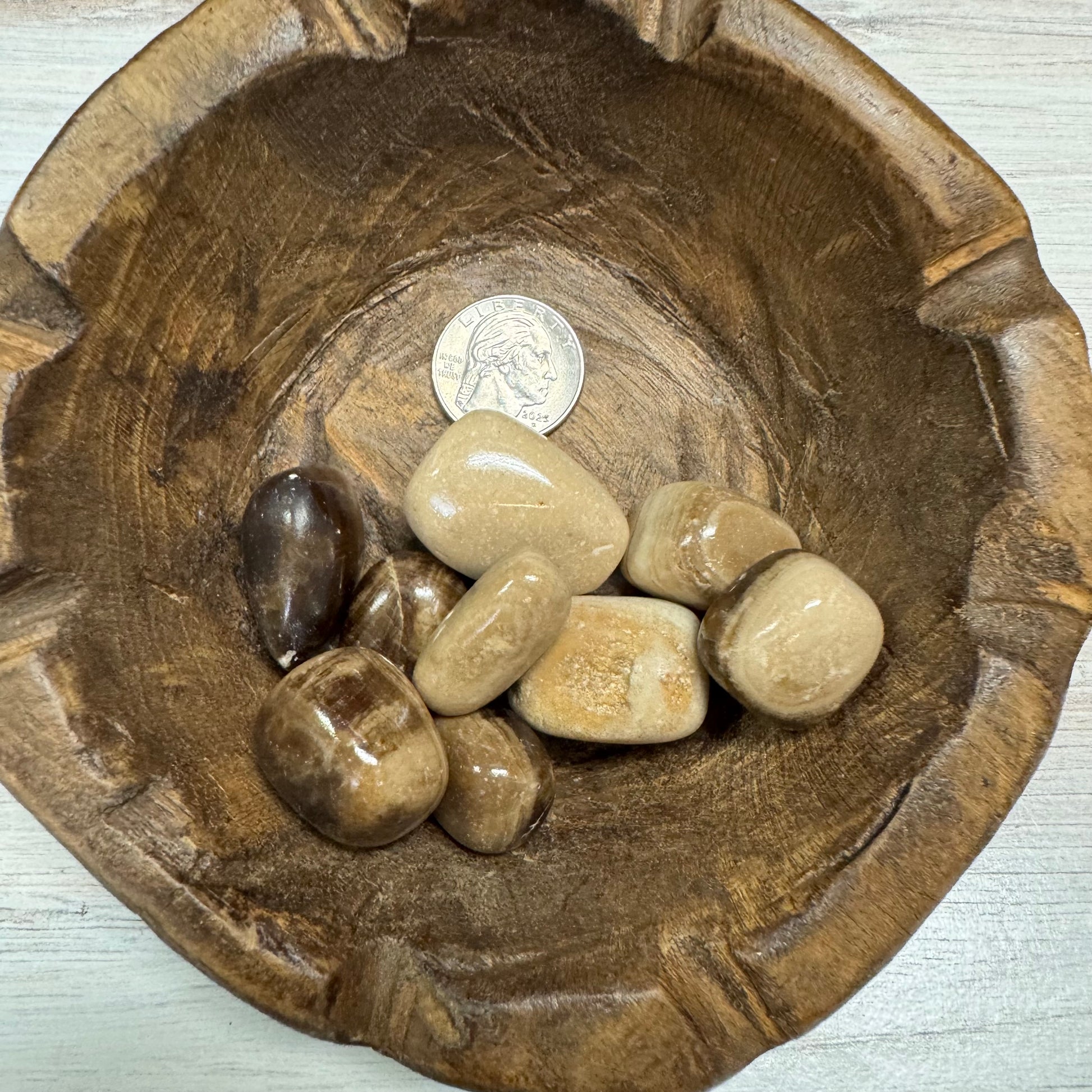 Wooden bowl with stones and a coin on a light wooden surface