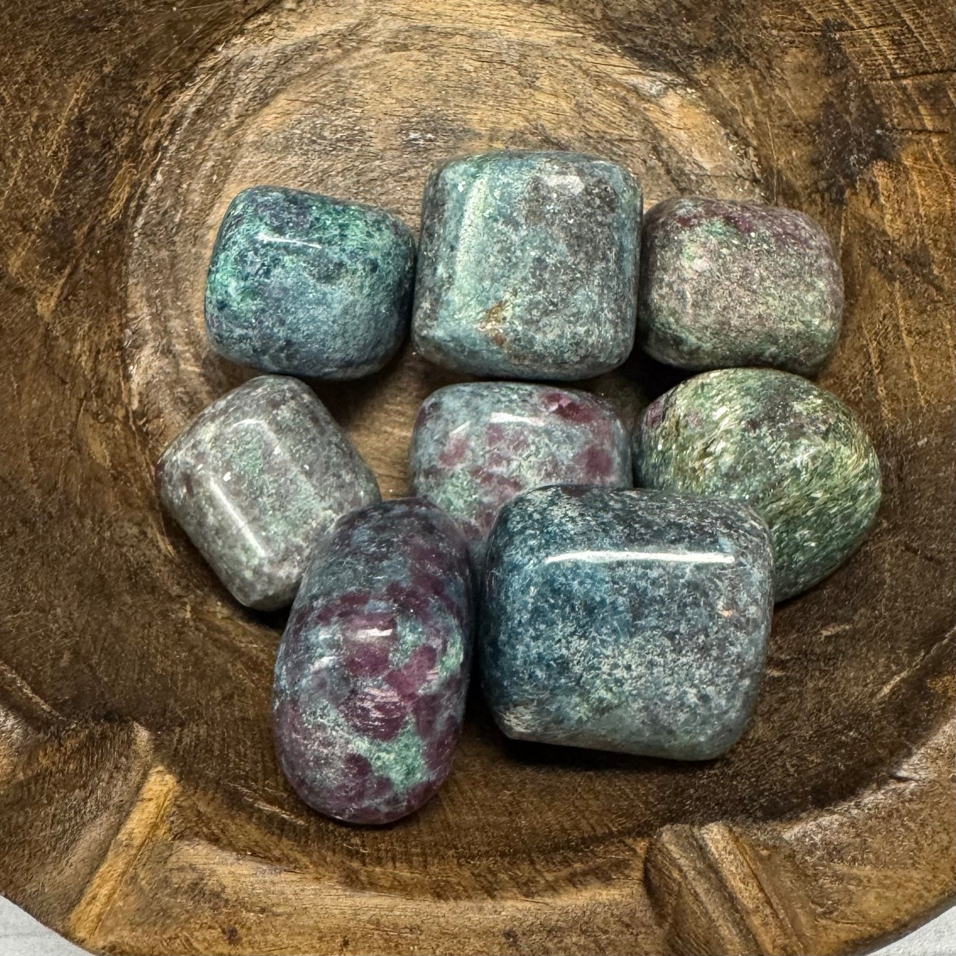 Collection of polished gemstones in a wooden bowl