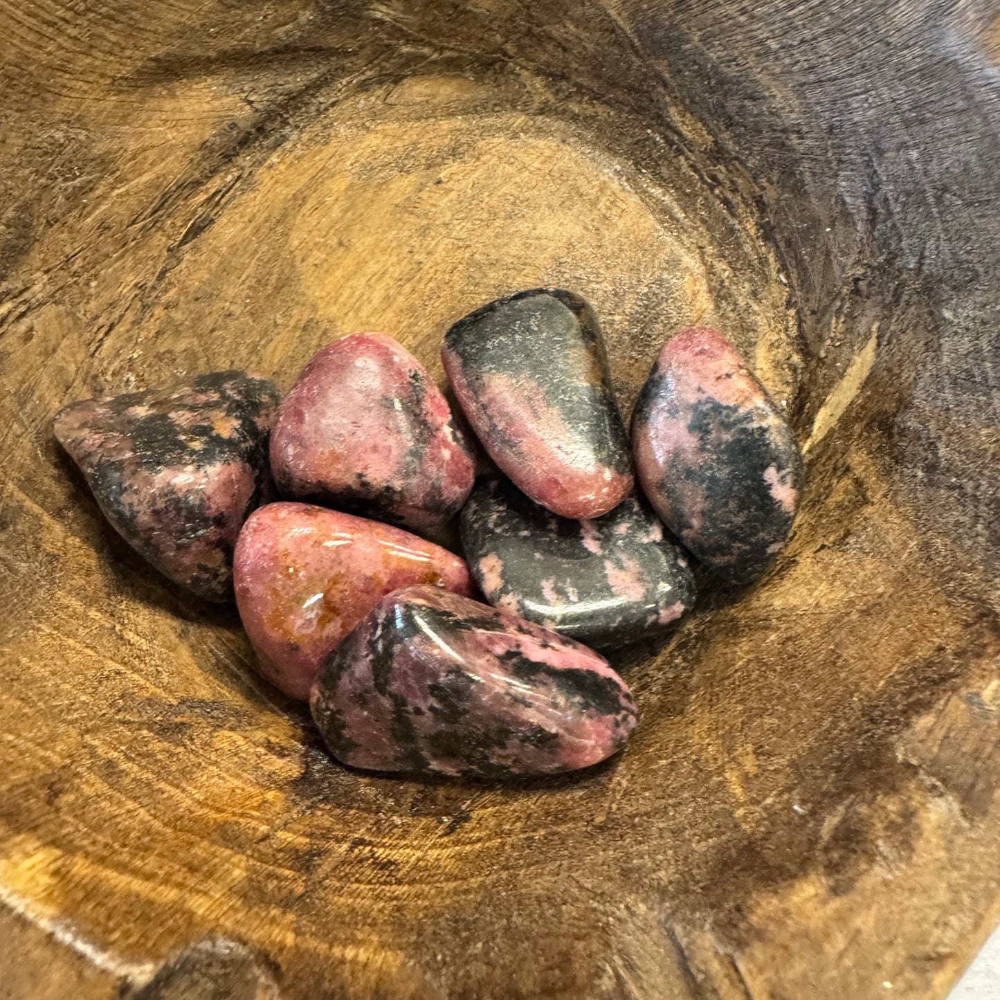 Polished rhodonite stones in a wooden bowl