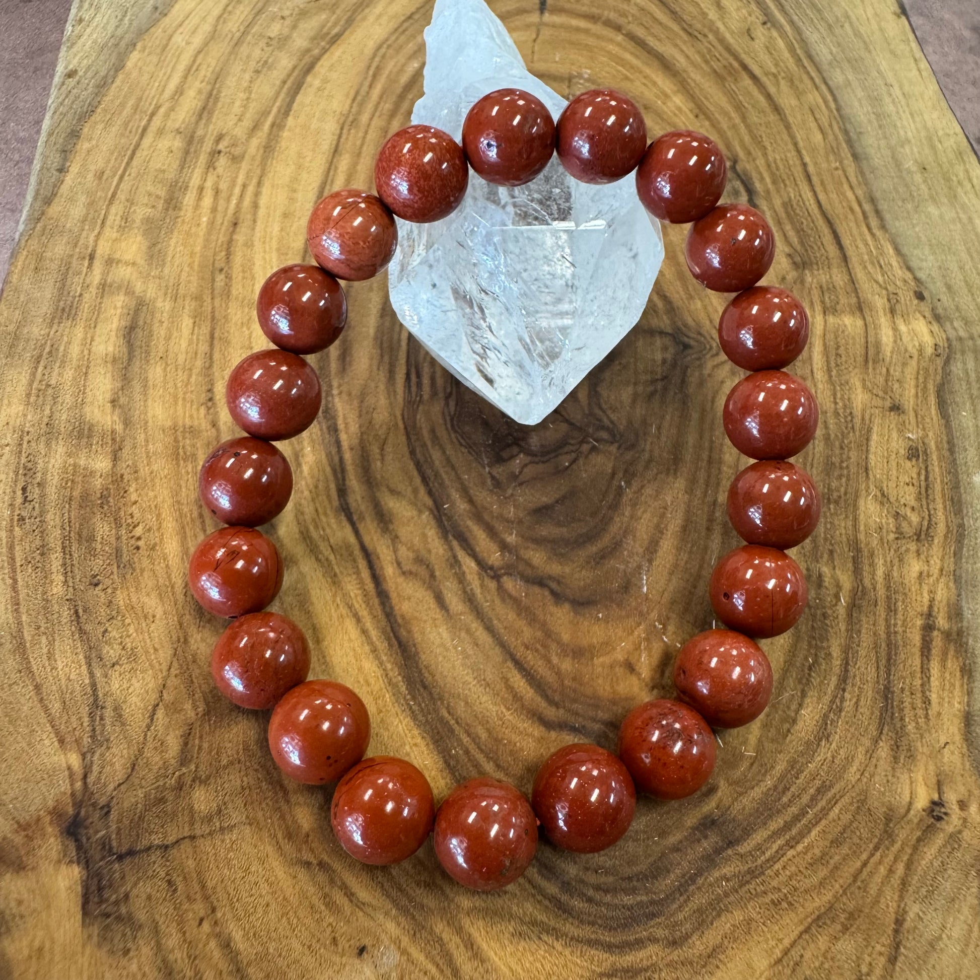 Red beaded bracelet on a wooden surface with a crystal stone