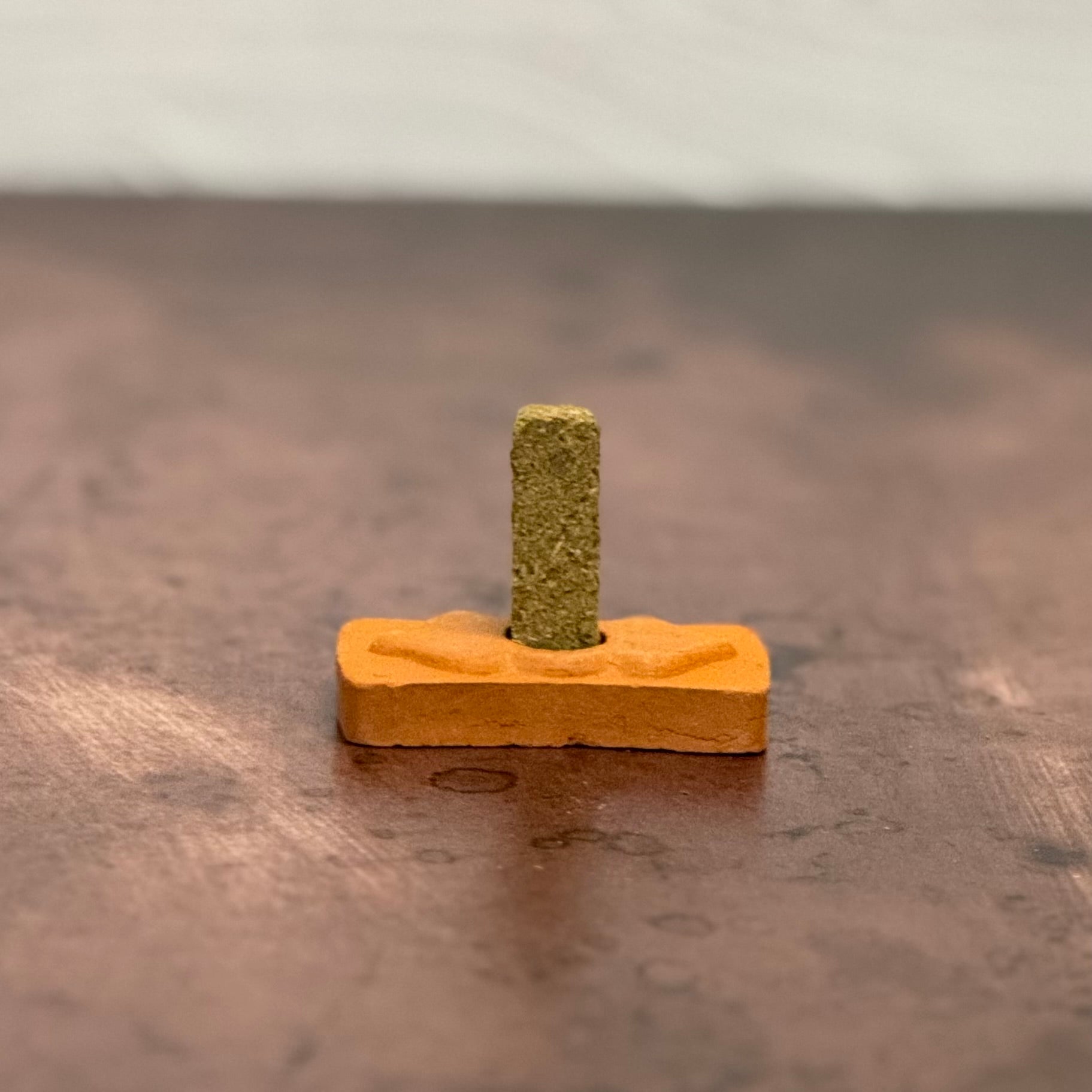 Small wooden block with a cylindrical green object on a reflective surface