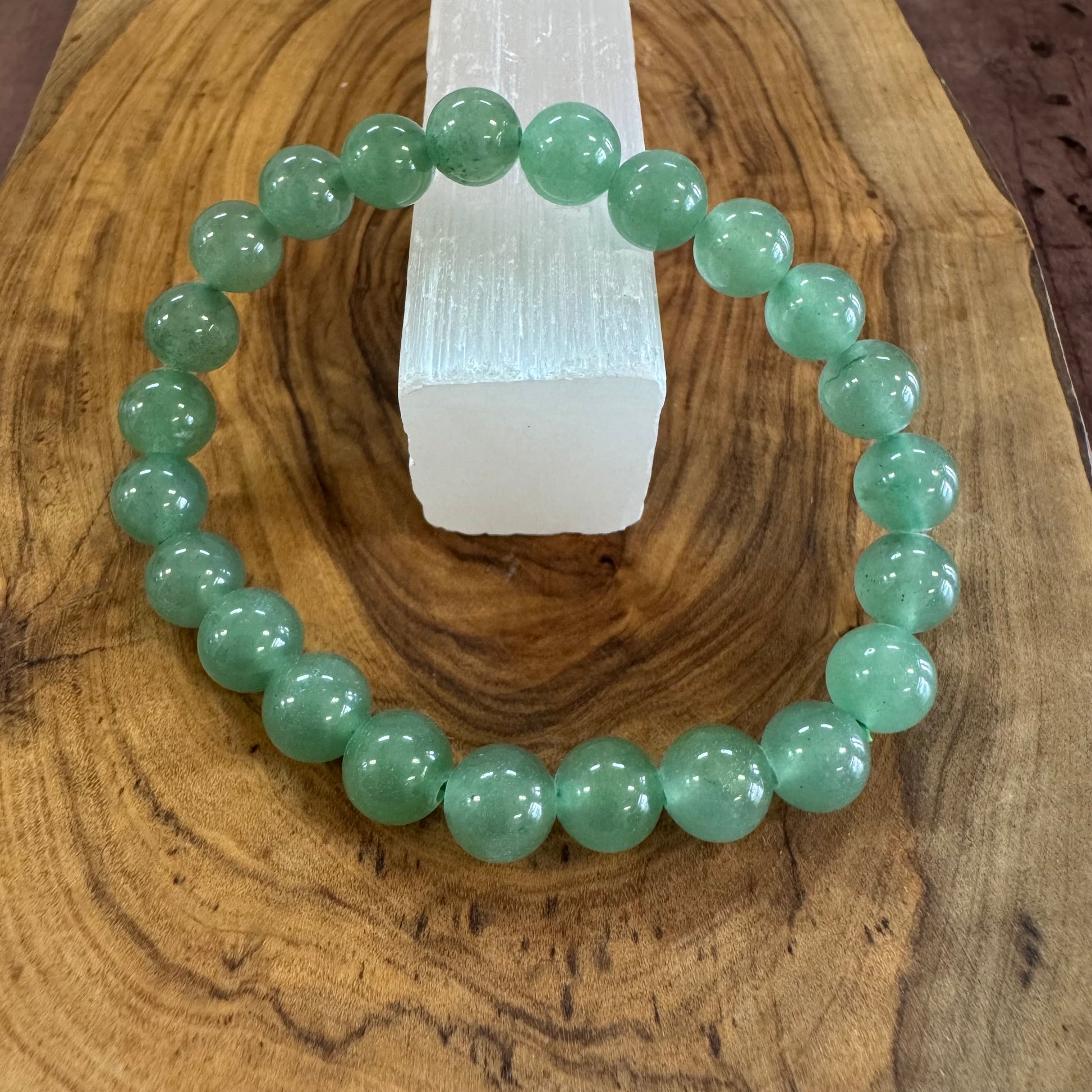 Green beaded bracelet on a wooden surface with a crystal in the background