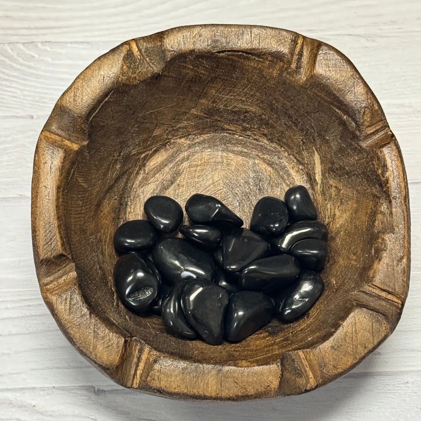 Wooden bowl with black stones on a light wooden surface