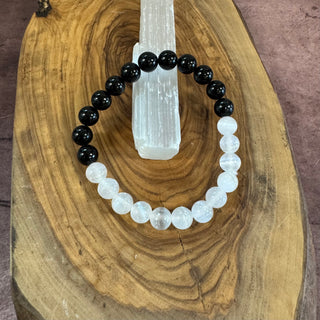 A beaded stretch bracelet with alternating black and white beads, displayed on a wooden slice with a white crystal cluster stand.
