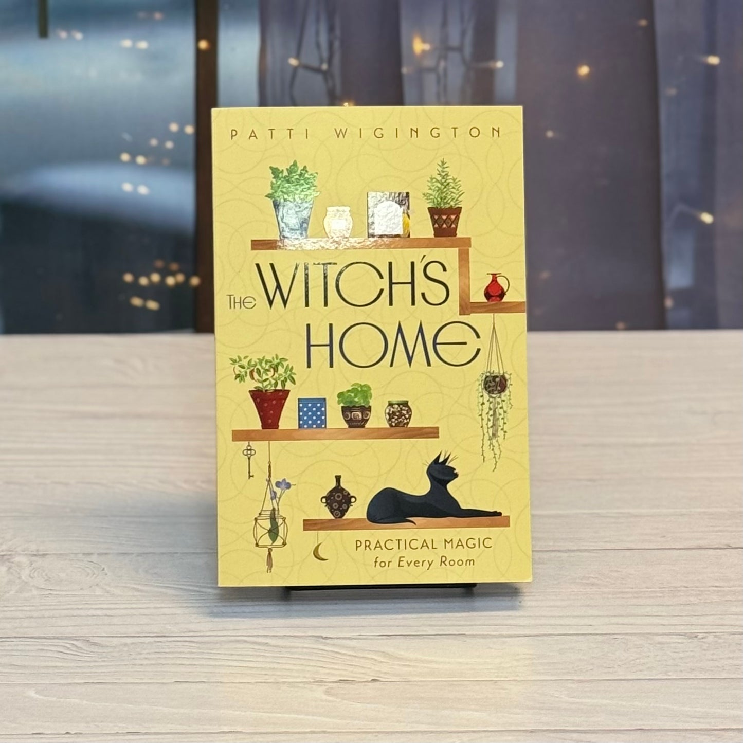 Book titled 'The Witch's Home' by Patti Wigington on a wooden surface with a blurred background.