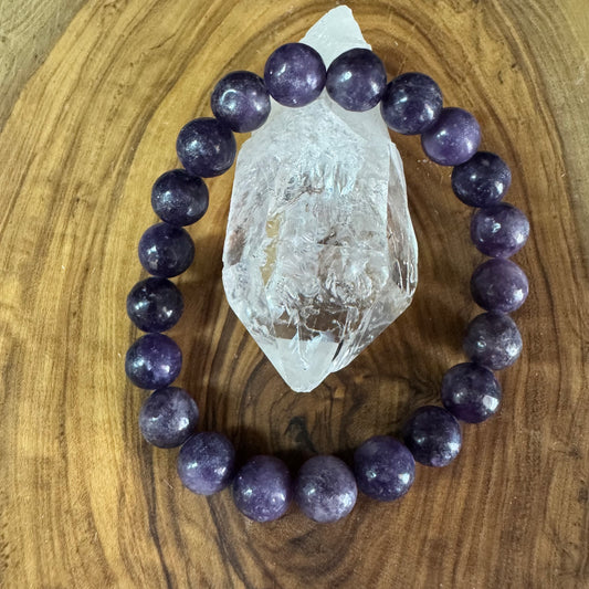 Purple beaded bracelet on a wooden surface with a crystal
