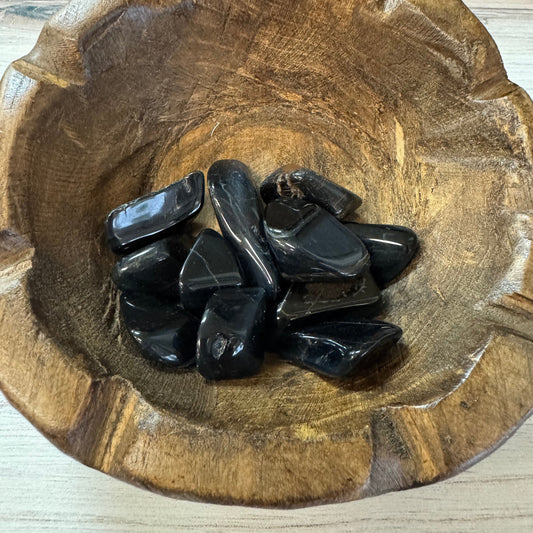Black stones in a wooden bowl on a light wood background