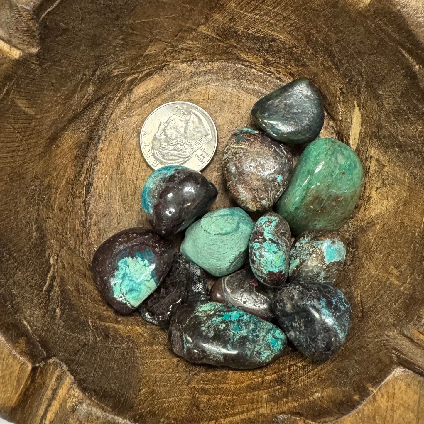 Turquoise stones in a wooden bowl with a coin for scale