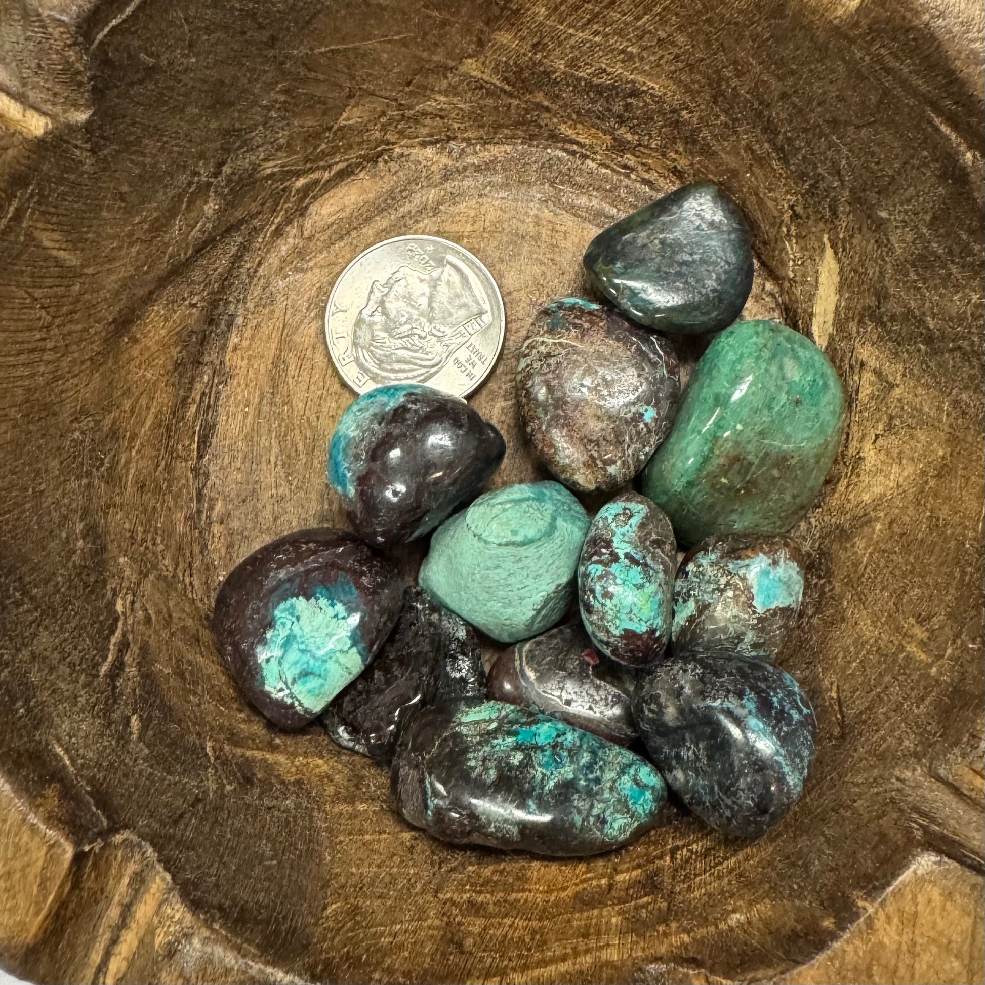 Turquoise stones in a wooden bowl with a coin for scale