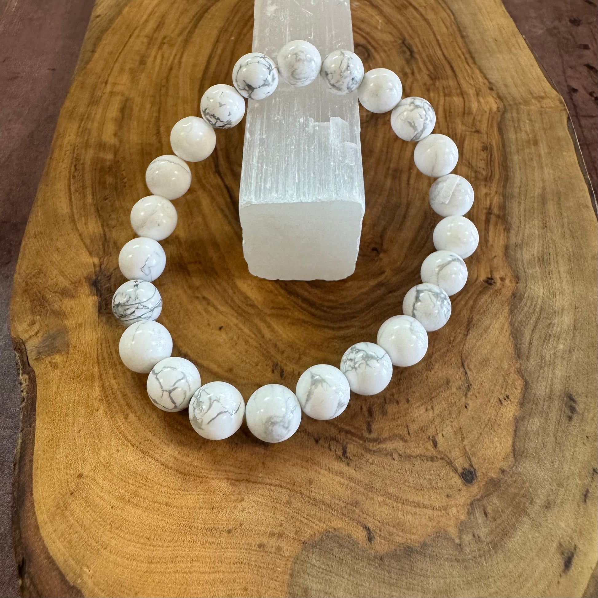 White marble beaded bracelet on a wooden surface with a crystal block.