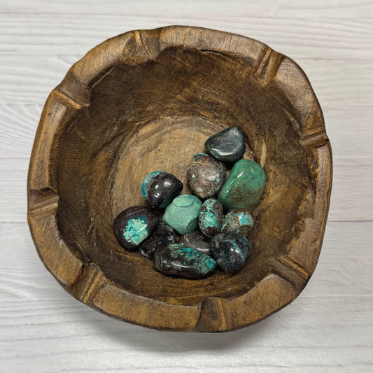 Wooden bowl with turquoise and black stones on a light wooden surface