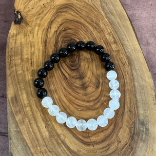 A beaded stretch bracelet with alternating black and milky white round beads, displayed on a rustic wood slice background.