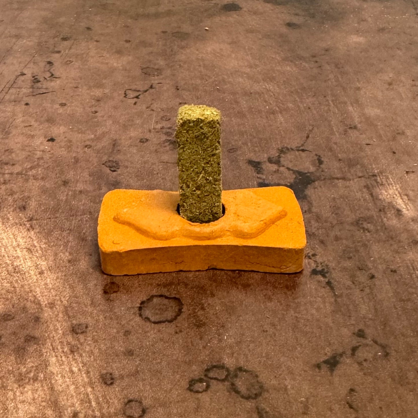 Yellow block with a green textured object on top, on a brown surface