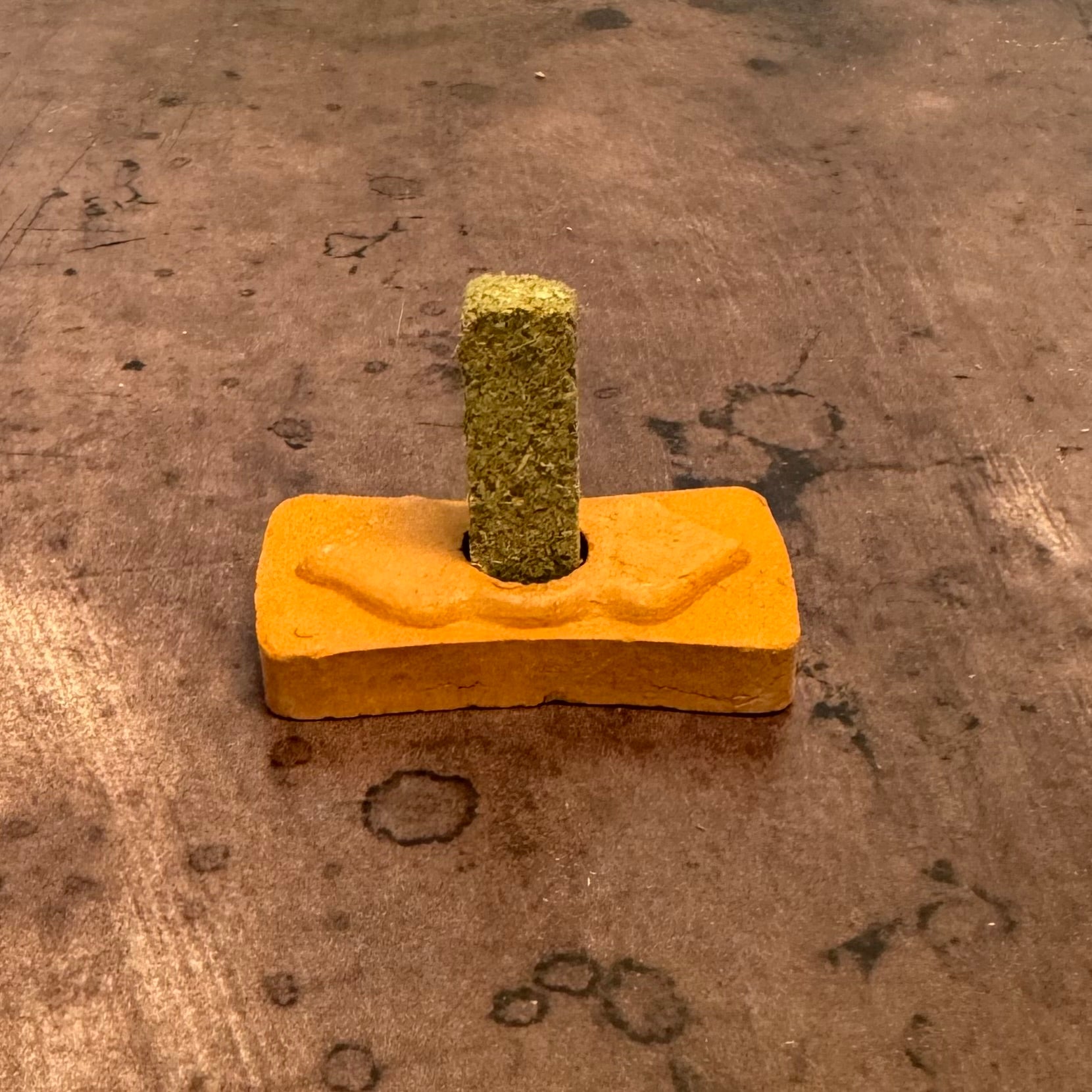 Yellow block with a green textured object on top, on a brown surface