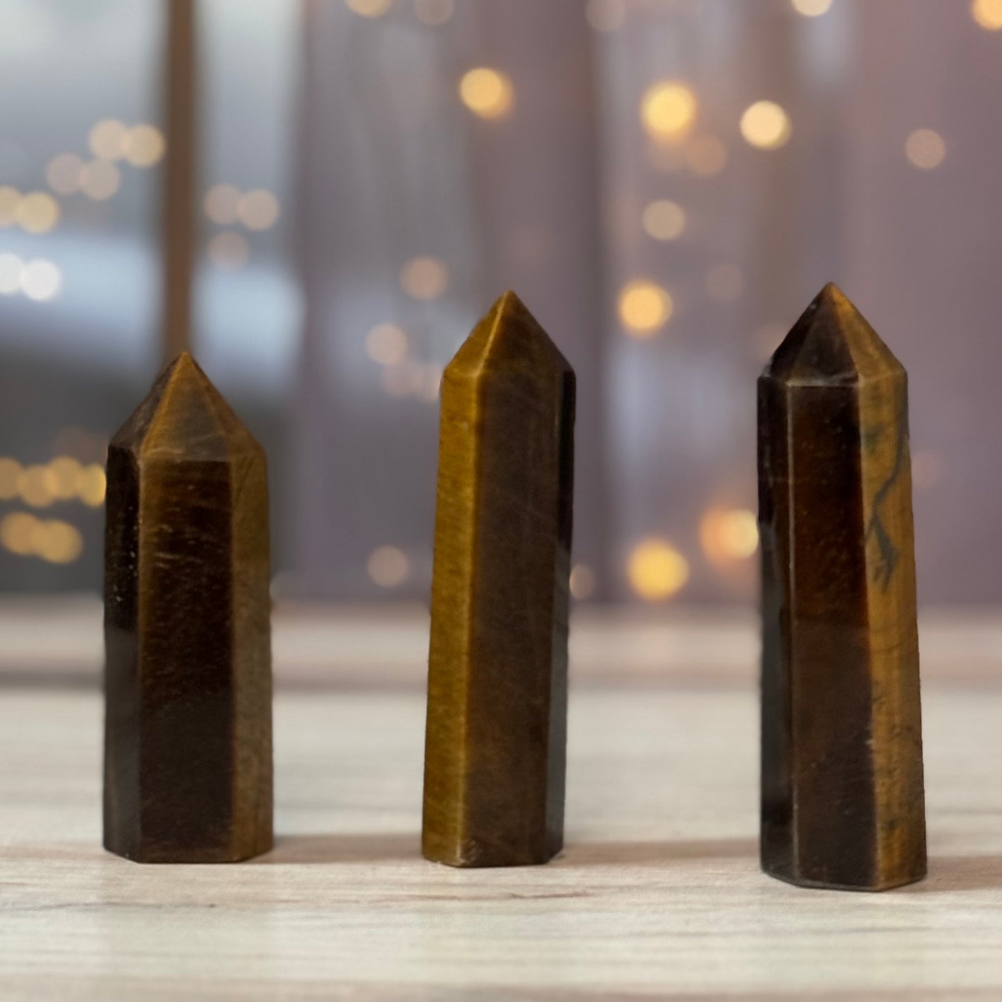 Three brown crystal points on a wooden surface with a blurred background of lights.