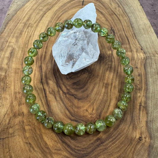 Green beaded bracelet on a wooden surface with a crystal