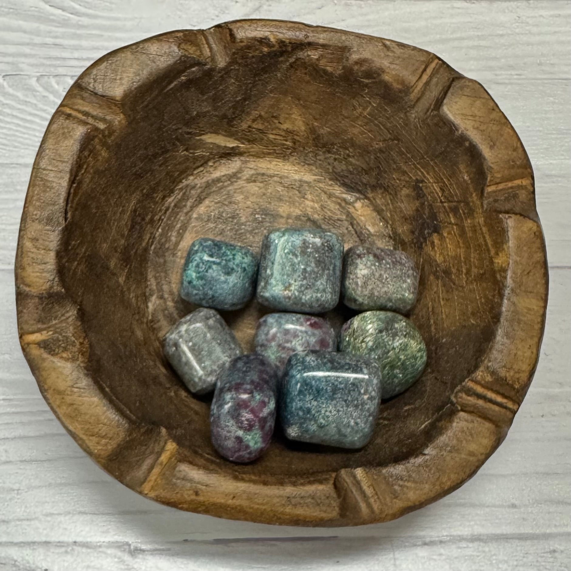 Wooden bowl with colorful stones on a light wooden surface