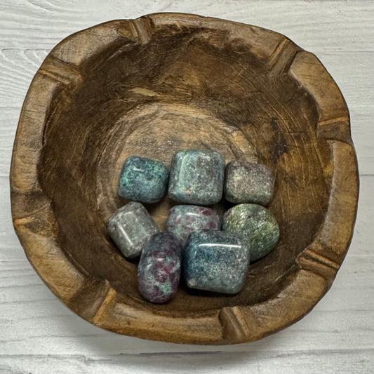 Wooden bowl with colorful stones on a light wooden surface