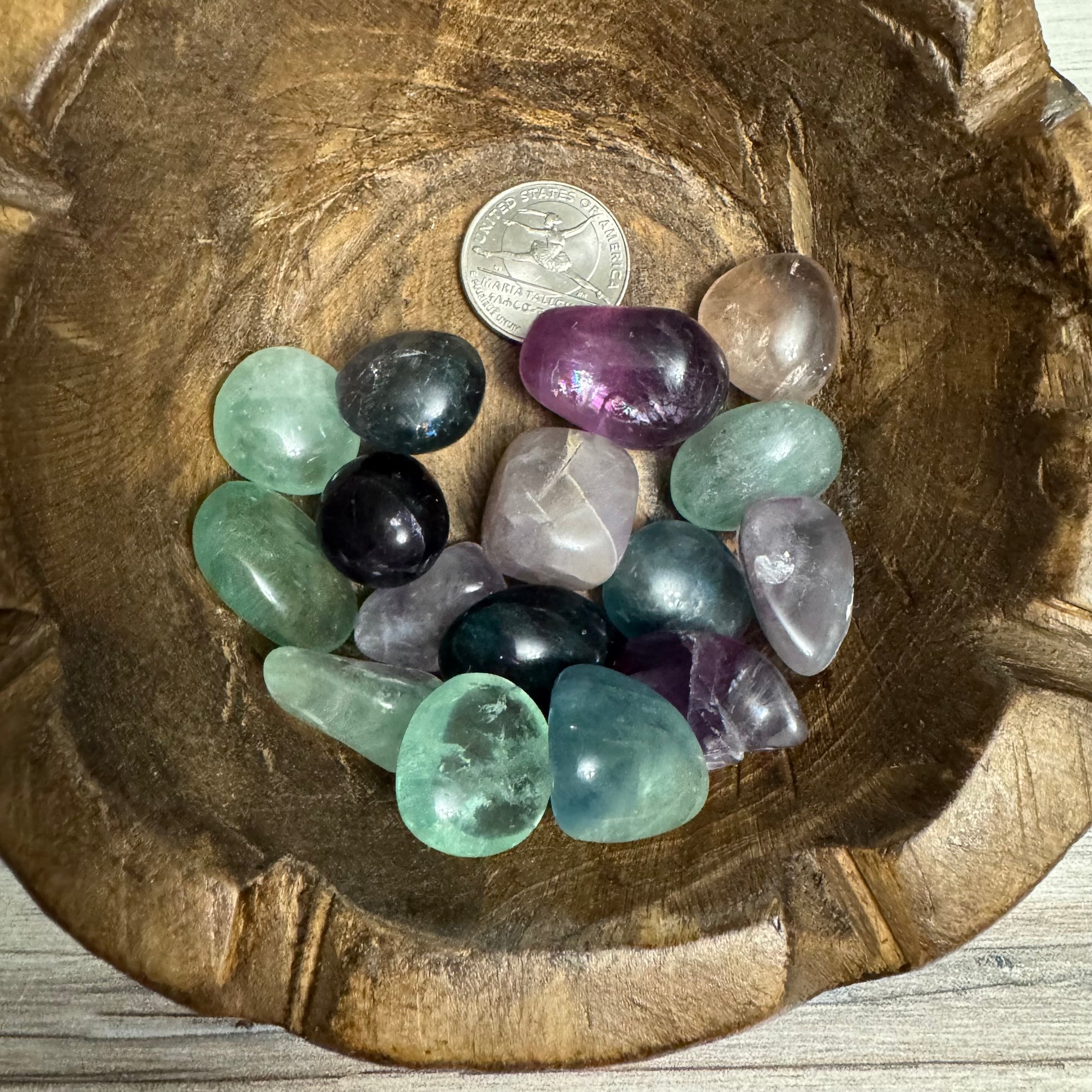 Assorted colorful crystals in a wooden bowl with a coin for scale.