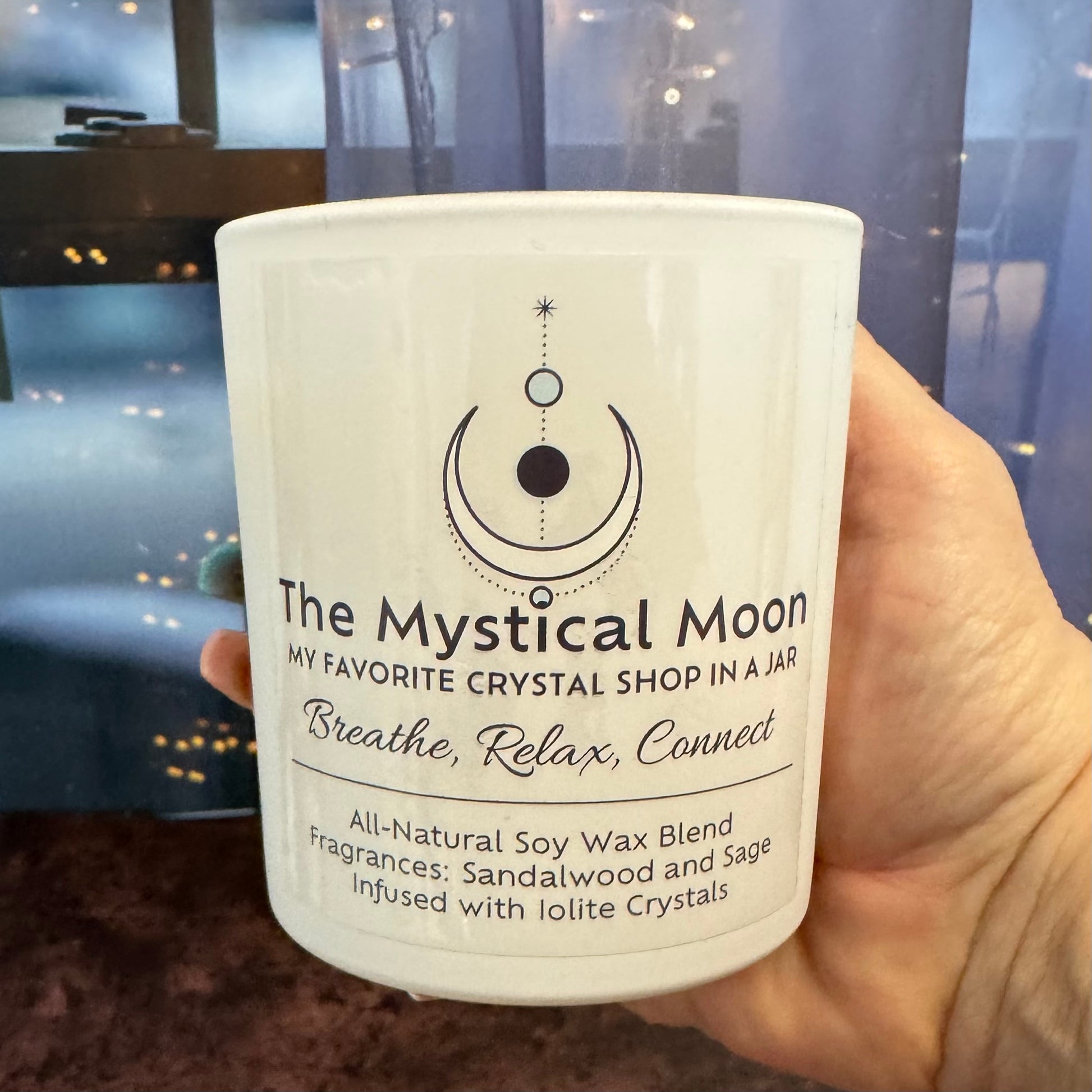 Candle in a white container labeled 'The Mystical Moon' held by a hand.