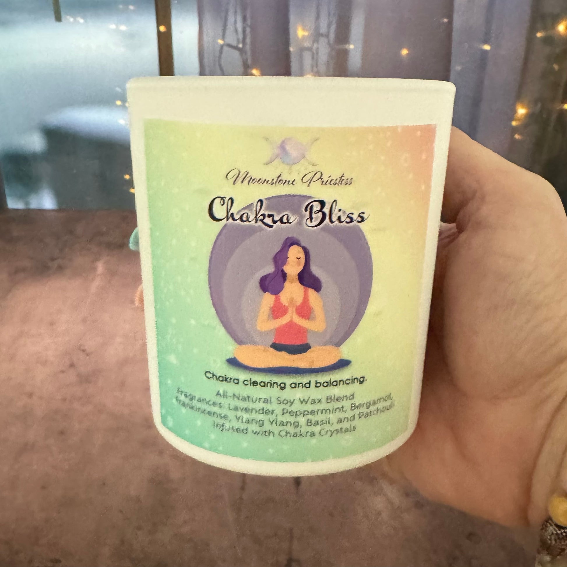 Hand holding a candle labeled 'Chakra Bliss' with a blurred background