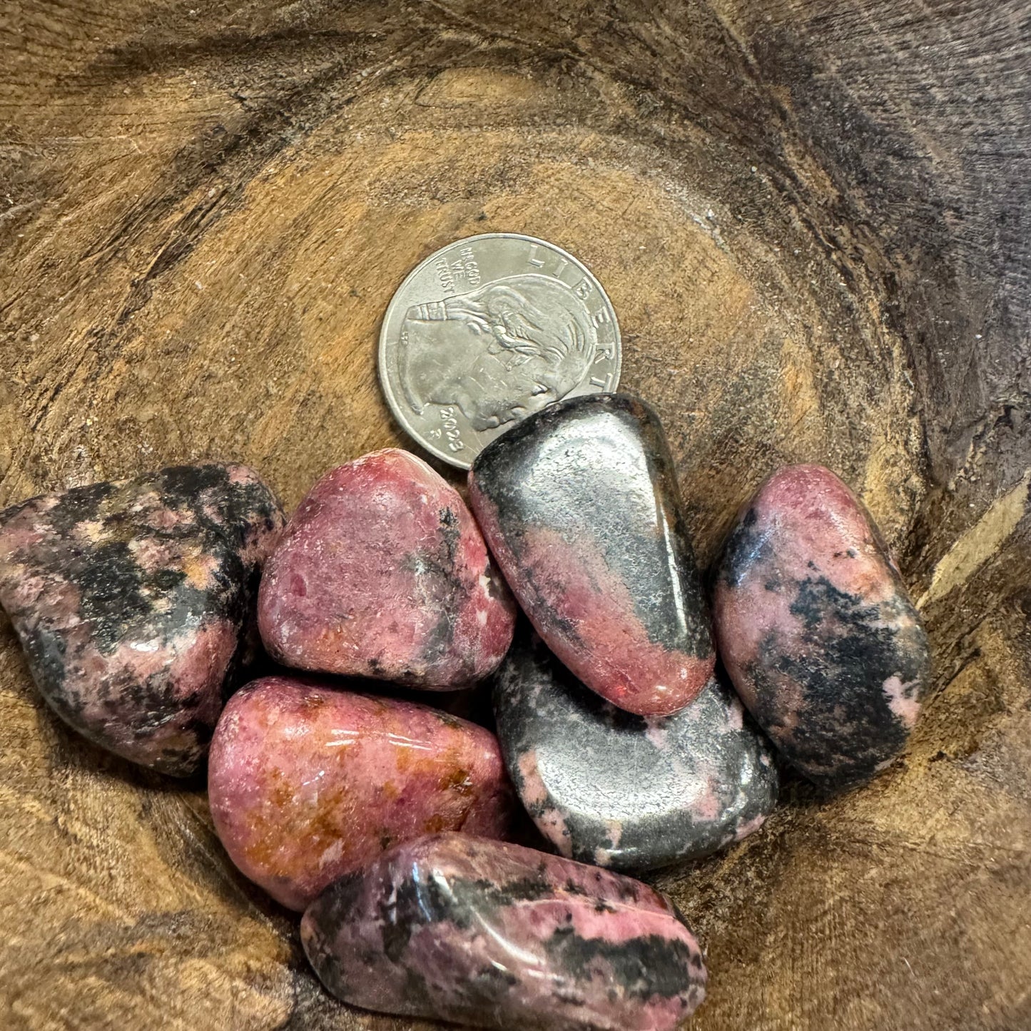 Polished rhodonite stones with a quarter for scale on a wooden surface