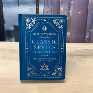 Blue book titled 'Classic Spells for Modern Times' by Silver Ravenwolf on a wooden surface with a blurred background.