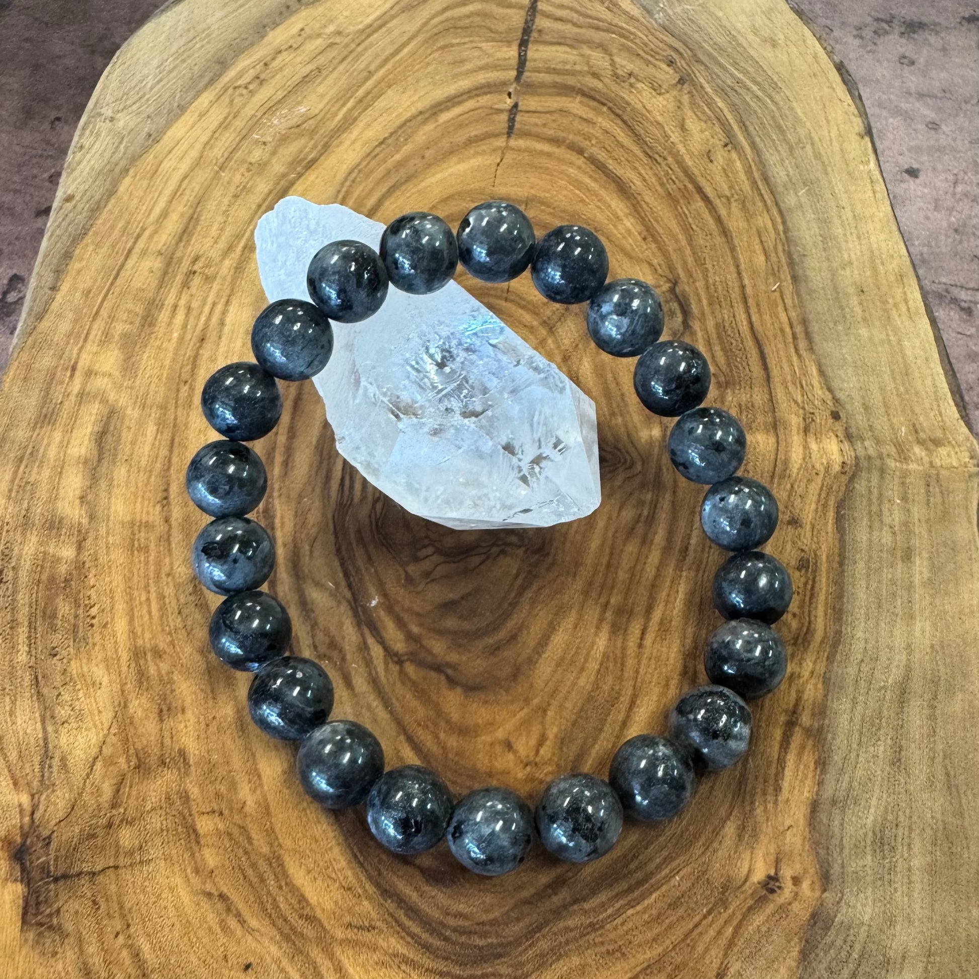 Black labradorite beaded bracelet on a wooden surface with a crystal