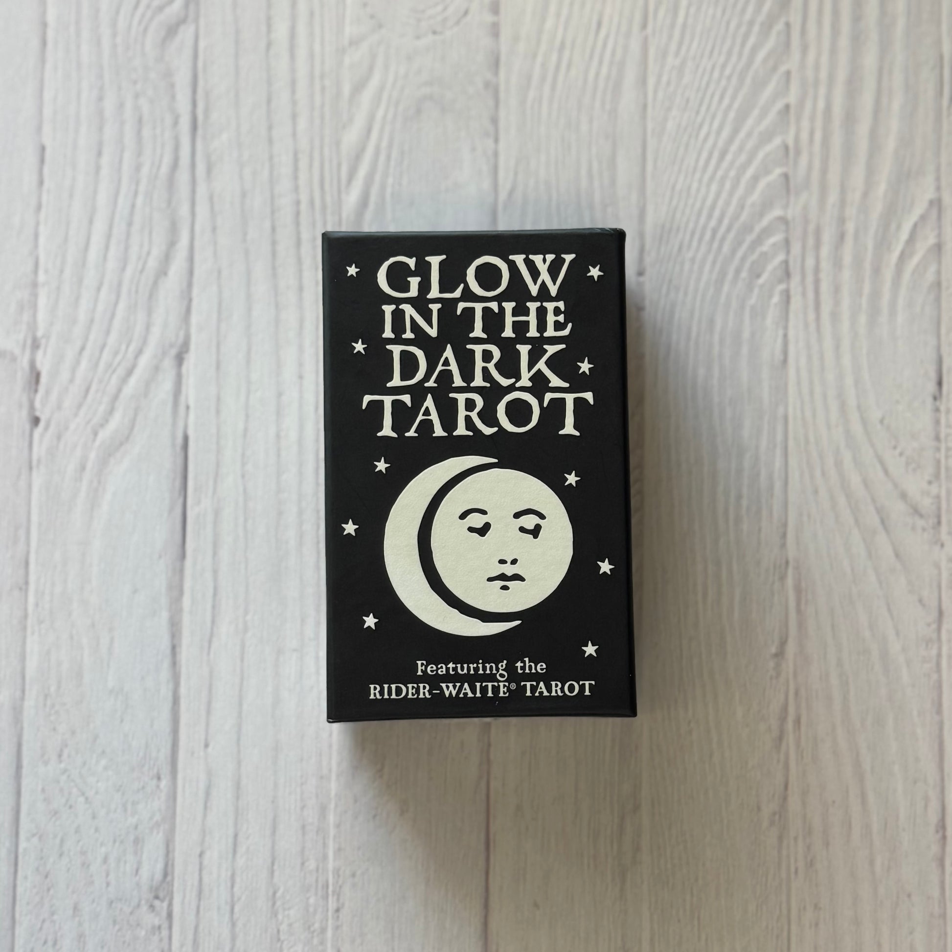 Glow in the Dark Tarot book with a moon and face design on a wooden surface