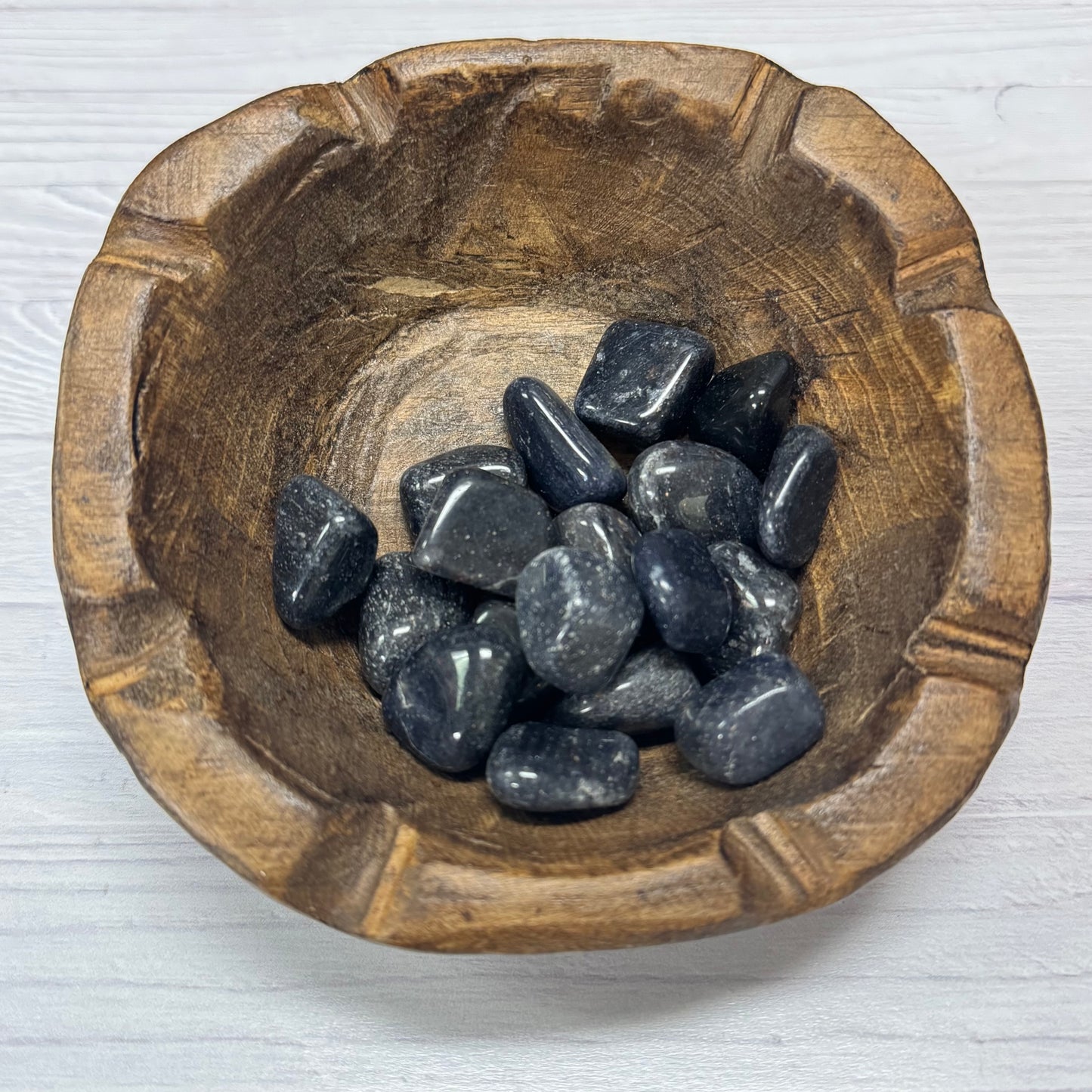 Wooden bowl filled with dark stones on a light wooden surface