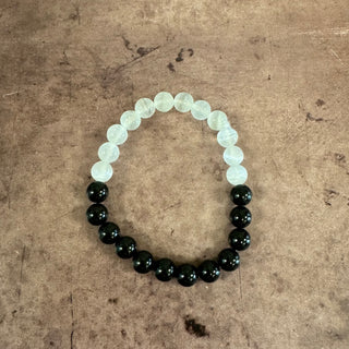 A beaded stretch bracelet made of alternating translucent pale green beads and glossy black round beads, displayed on a textured brown surface.