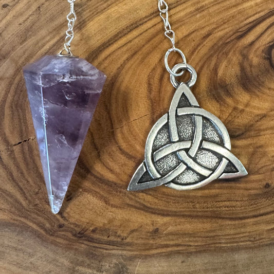 Silver Celtic knot pendant and amethyst crystal on a wooden surface
