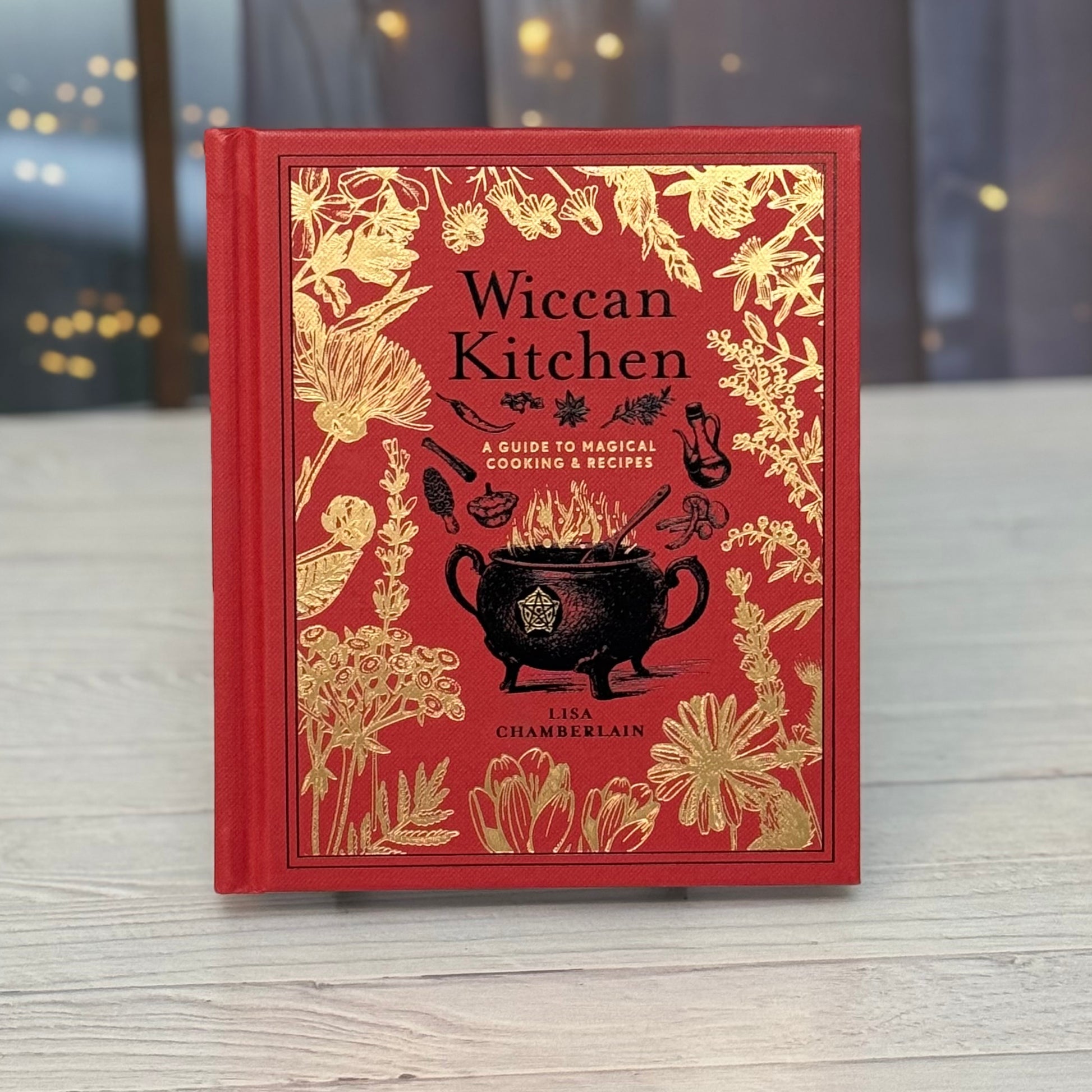 Red book titled 'Wiccan Kitchen' with gold illustrations on a wooden surface.
