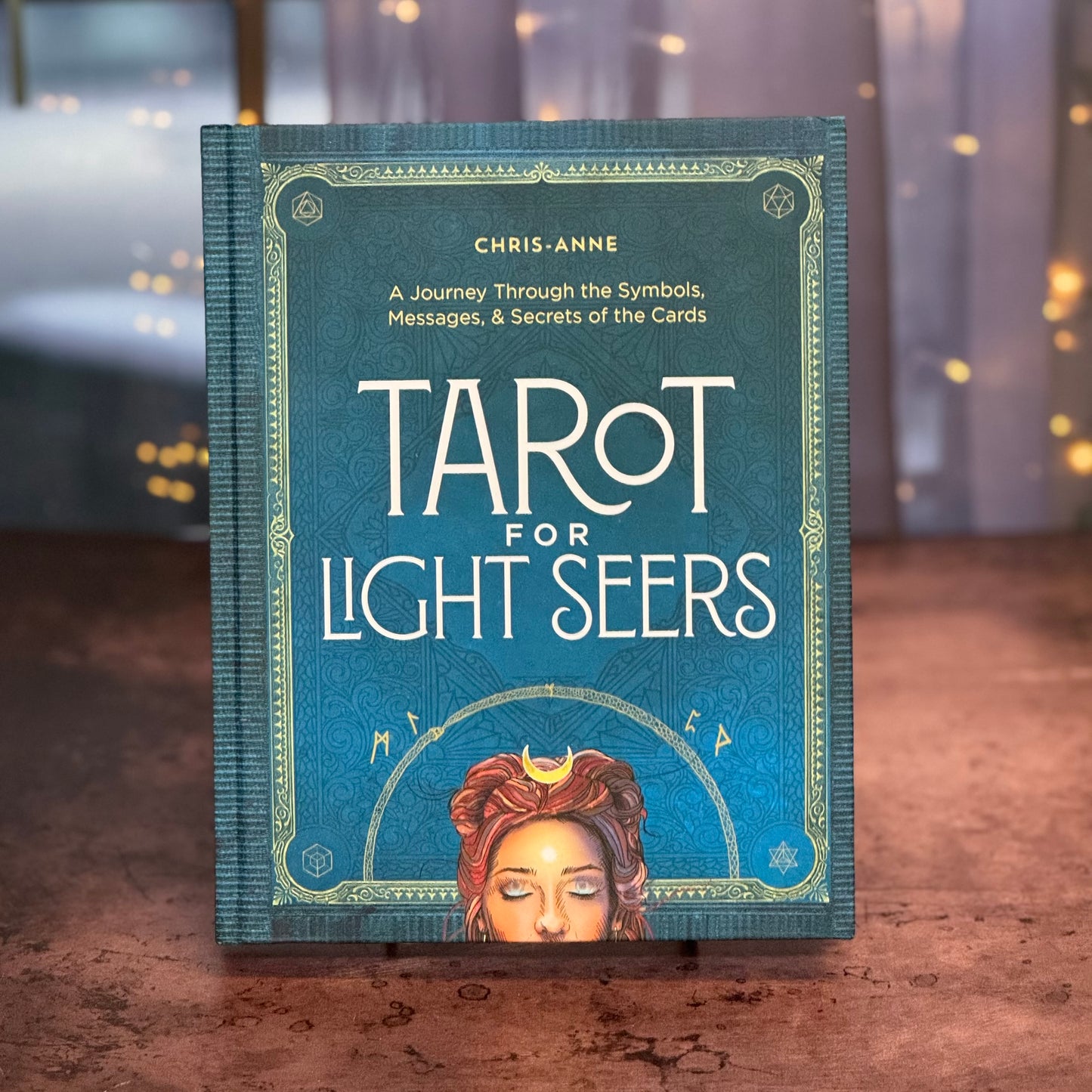 Book titled 'Tarot for Light Seers' by Chris Anne on a wooden surface with blurred lights in the background