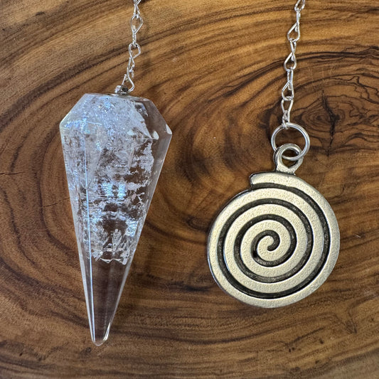 Crystal pendulum and spiral pendant on a wooden surface
