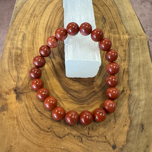 Red beaded bracelet on a wooden surface with a crystal in the background