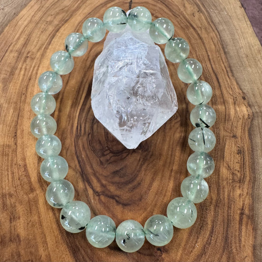 Green beaded bracelet on a wooden surface with a crystal rock