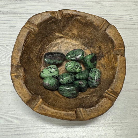 Wooden bowl with green stones on a light wooden surface