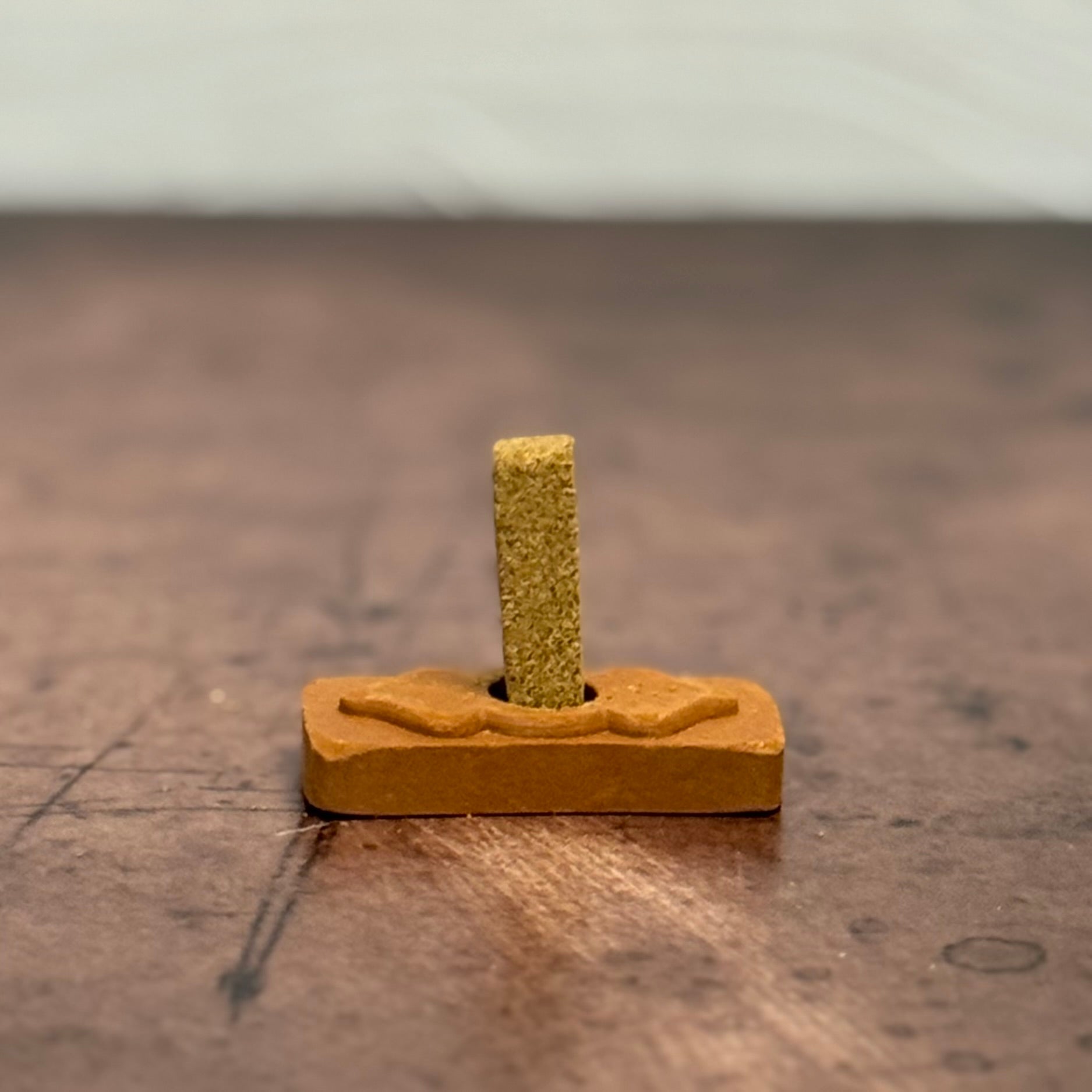 Small wooden block with a cylindrical green object on a wooden surface