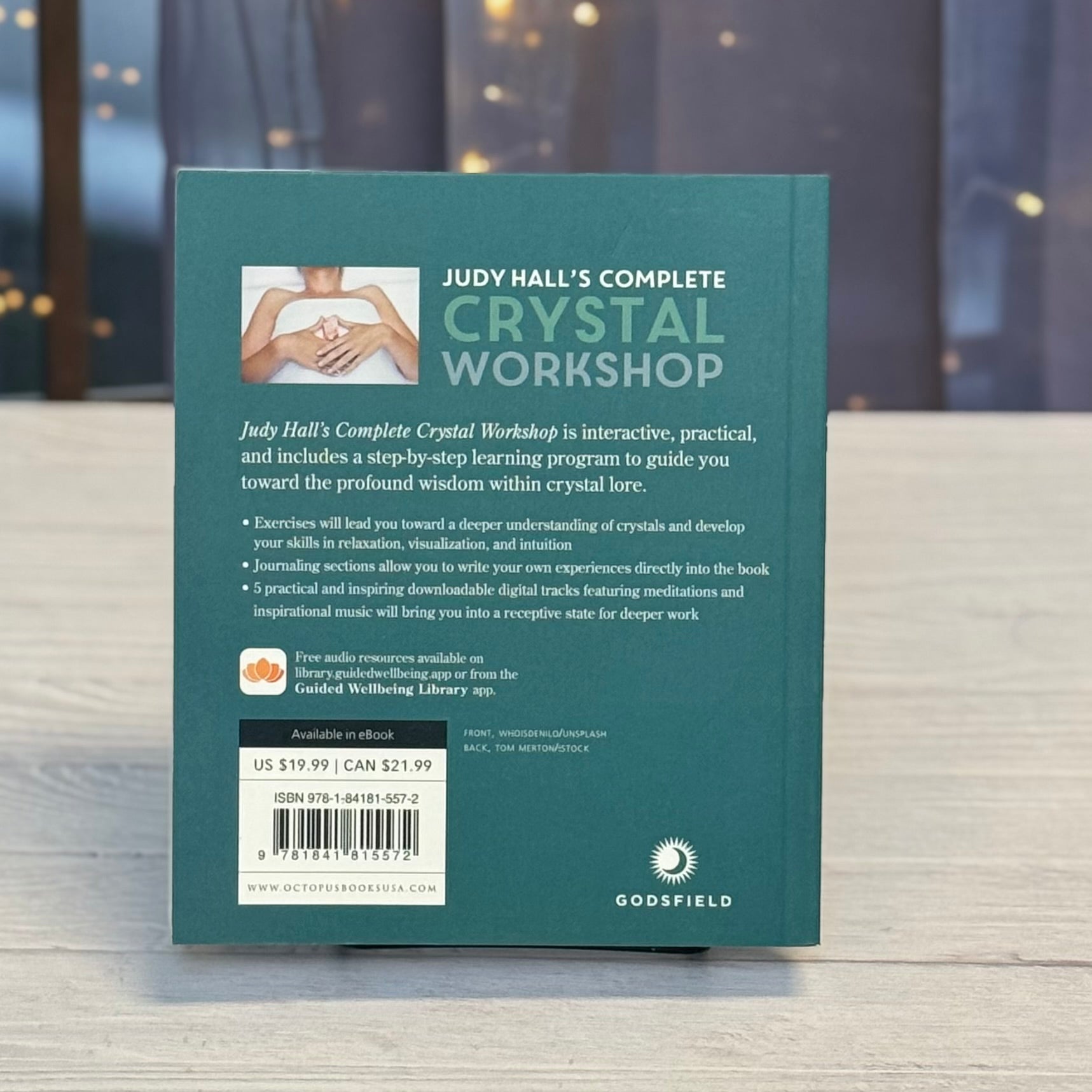 Book titled 'Judy Hall's Complete Crystal Workshop' on a wooden surface with a blurred background