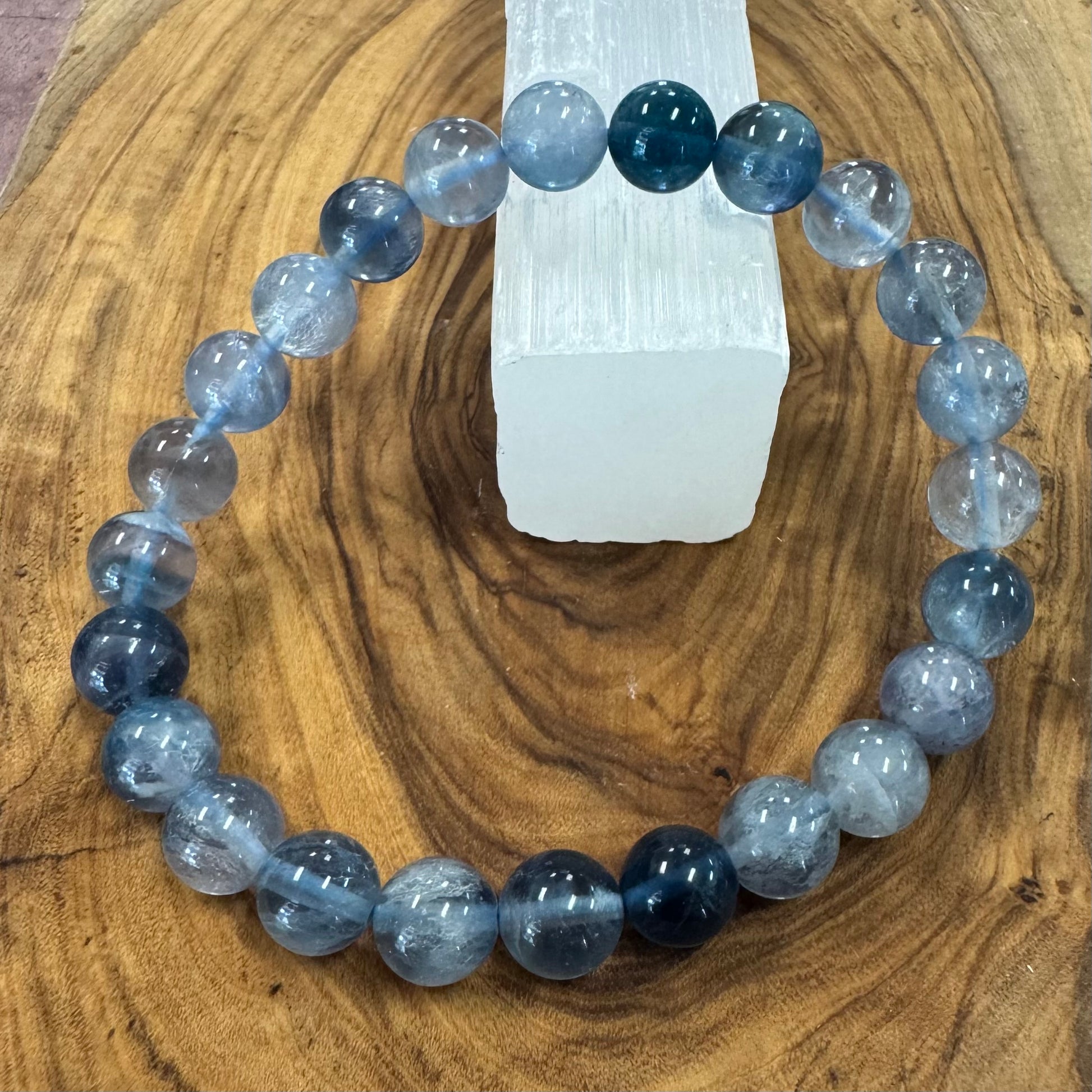 Blue and gray beaded bracelet on a wooden surface with a crystal in the background