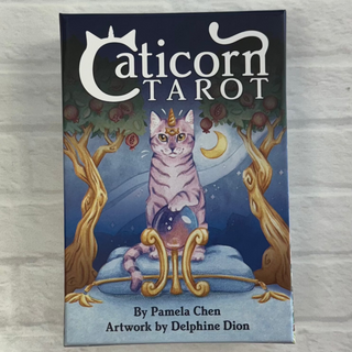 The image features the cover of the Caticorn Tarot deck, which is illustrated by Pamela Chen and has a title and artwork describing a mythical cat kingdom. The cover shows a cute, cartoon-style cat with a crown sitting on a throne under a moonlit tree, with a background suggesting a mystical, forest-like setting.