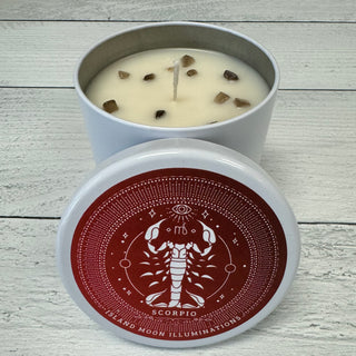 A Scorpio Zodiac themed candle with black violet, bonfire, and vanilla fragrances, and smoky quartz crystals, displayed in a white container with a red label.