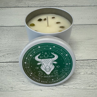 An 11 oz Taurus Zodiac themed candle with fig, jasmine, and white tea fragrance, and green garnet crystals. The candle is placed in a white container with a green and white label featuring the Taurus sign and zodiac symbols.