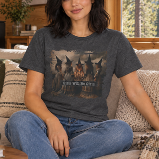 A woman sitting on a couch wearing a dark gray graphic t-shirt with a witch illustration and the text 'Girls Will Be Girls.'