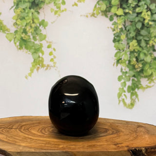 Black decorative object on a wooden surface with green foliage in the background