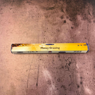 A long, narrow yellow box labeled 'Money Drawing' lies horizontally on a worn, dusty brown surface.