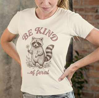 Person wearing a t-shirt with a raccoon graphic and 'Be kind... of feral' text.